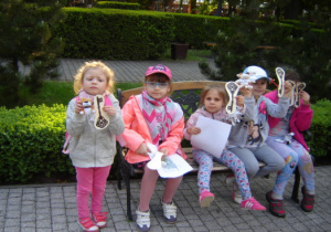 Dzieci siedzą na ławce w Ogrodzie Pałacu Poznańskiego i pokzują swoje klucze.
